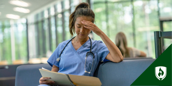 A nurse in blue scrubs sits in a hospital lounge looking at a case file