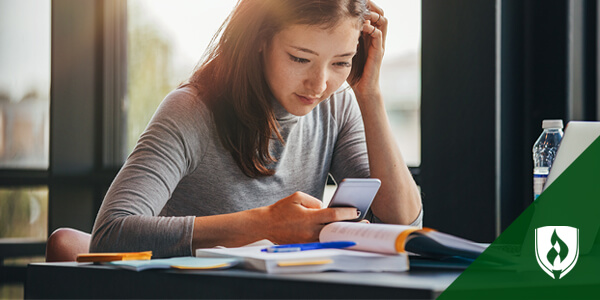 female student looking at smartphone while studying
