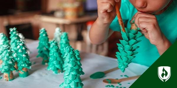 illustration of toddler painting wooden christmas trees representing winter activities for preschoolers