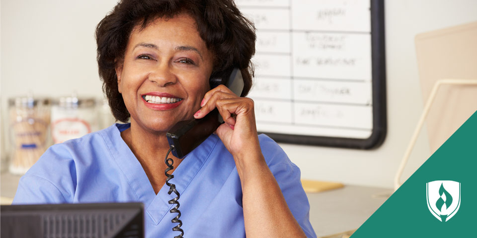 female nurse in scrubs behind desk talking on phone