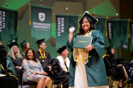 Waving Rasmussen University graduate with diploma at commencement ceremony