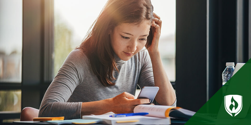 female student looking at smartphone while studying