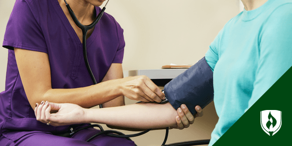 image of a medical assistant in scrubs manually taking a patient's blood pressure with a cuff and a stethascope representing medical assistant training