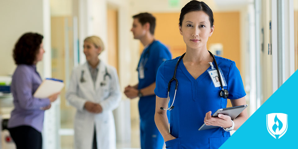 female nurse standing hallway with tablet in hand and co-workers behind