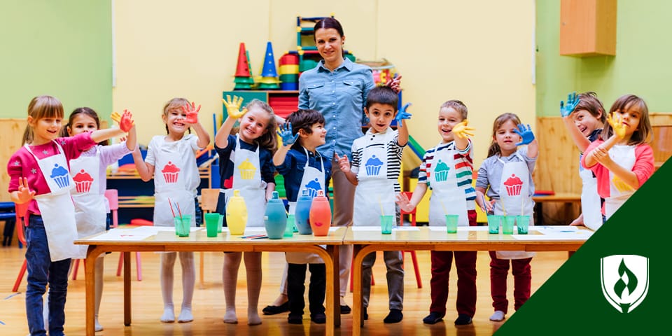 Teacher standing at table with a row of children working on an art project.