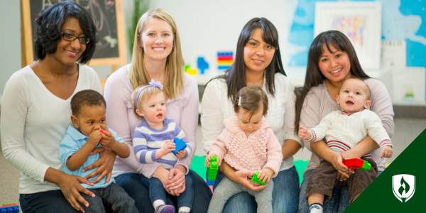Four ECE teachers sit with toddlers in their laps in a daycare classroom environment