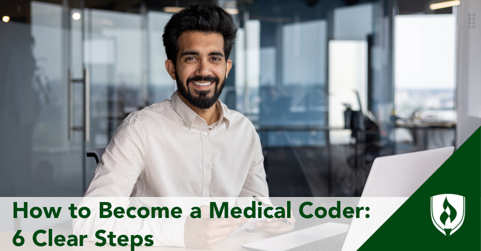 A medical coder holding a notebook smiles in front of his computer