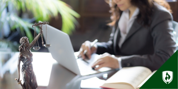 A statue of justice in the foreground of a paralegal working on a computer
