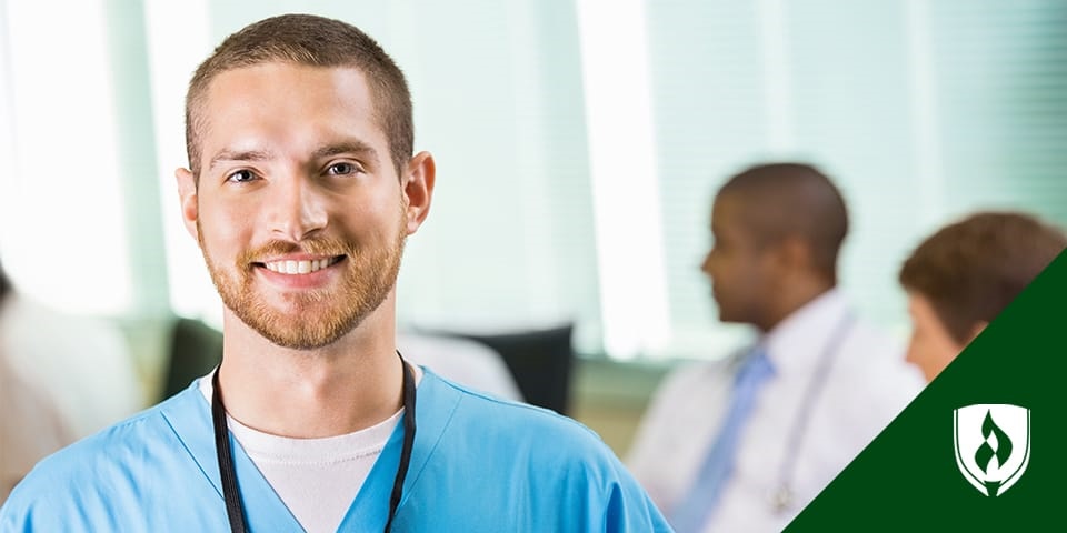 male nurse in scrubs standing by a nurses station