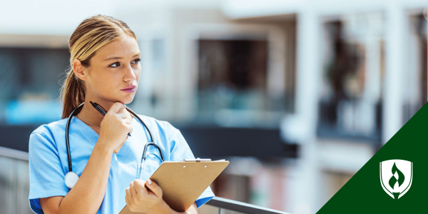 A female nurse thinks while looking off into the distance with a clipboard and pen
