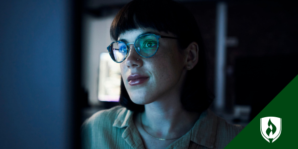 A white, female data science student with glasses looks into the blue light of a computer
