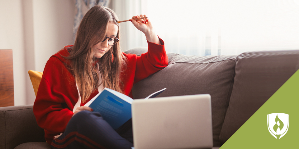 Female student studying on a couch with a book and laptop