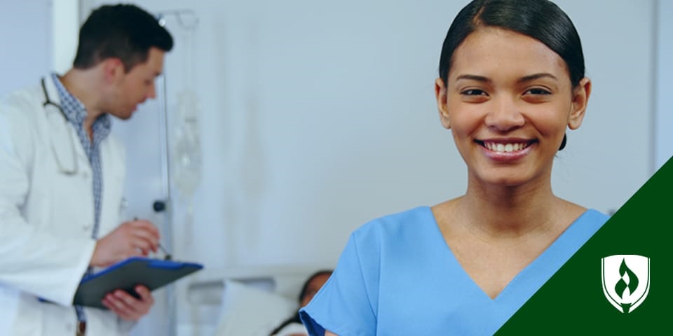 photograph of a smiling nurse in scrubs standing in front of a patient