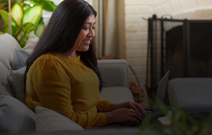 smiling woman sitting on couch in front of computer